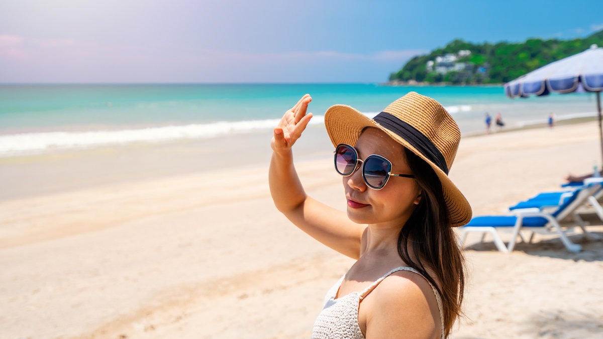 Young woman traveler wearing sunglasses covering face by hand to protect UV rays from the sun at tropical sandy beach on sunny day, Skin care and eyes protect concept 防曬營養素